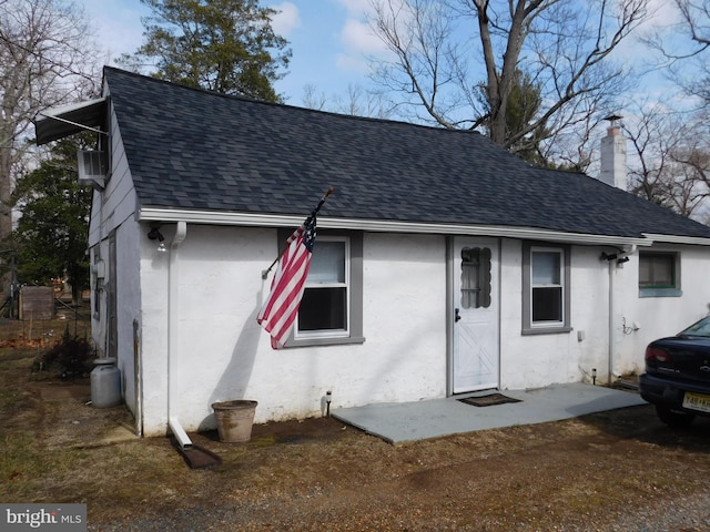 view of front of property with a shingled roof, a chimney, and stucco siding