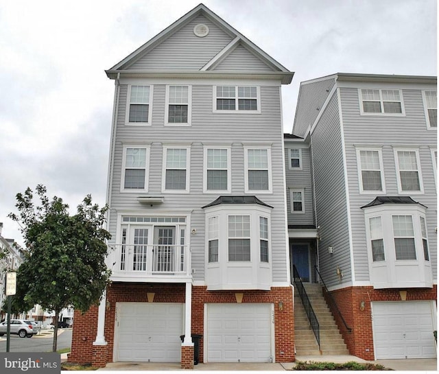 multi unit property featuring an attached garage, stairway, concrete driveway, and brick siding