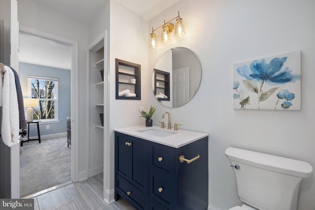 bathroom featuring built in shelves, baseboards, vanity, and toilet