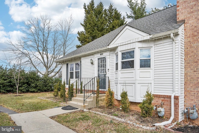 view of front of home featuring a front yard, brick siding, a chimney, and roof with shingles