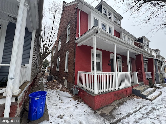 view of snow covered exterior featuring a porch, central AC unit, and brick siding