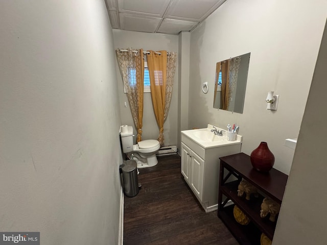 half bath with a baseboard heating unit, vanity, wood finished floors, and toilet