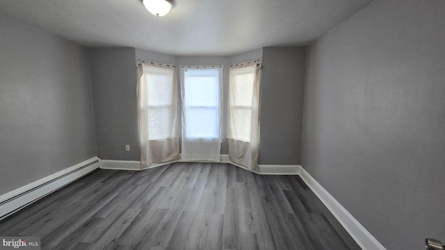 unfurnished room featuring baseboards, baseboard heating, and dark wood-type flooring