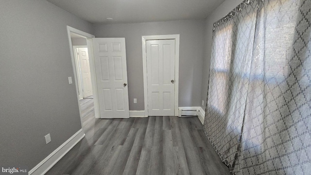 unfurnished bedroom with dark wood-type flooring, a baseboard radiator, and baseboards