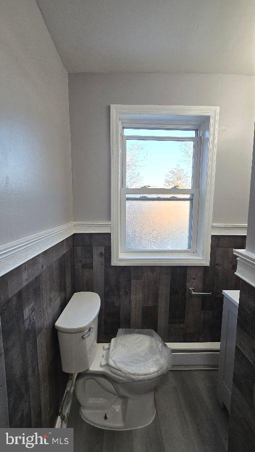 half bathroom with toilet, wooden walls, wood finished floors, and wainscoting