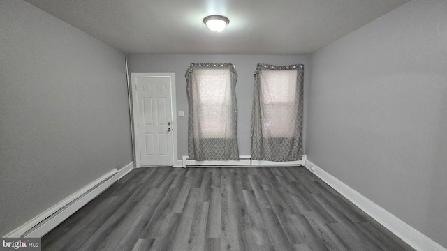 empty room featuring a baseboard radiator, baseboards, and dark wood-type flooring