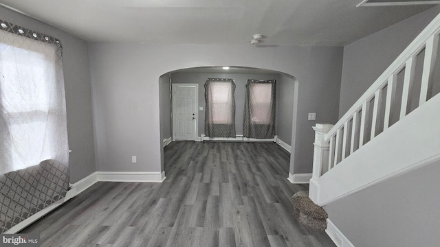 foyer with arched walkways, stairway, wood finished floors, and baseboards