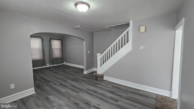 foyer entrance with dark wood-type flooring, arched walkways, stairway, and baseboards