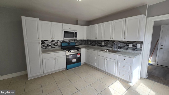 kitchen with light tile patterned floors, tasteful backsplash, white cabinets, stainless steel gas range, and a sink