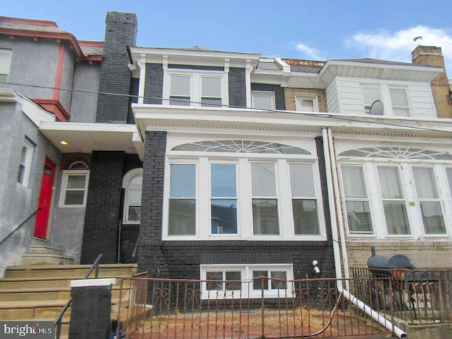 multi unit property featuring a fenced front yard, a chimney, and brick siding