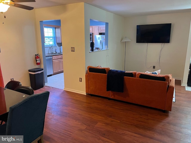 living room with a ceiling fan, baseboards, and wood finished floors