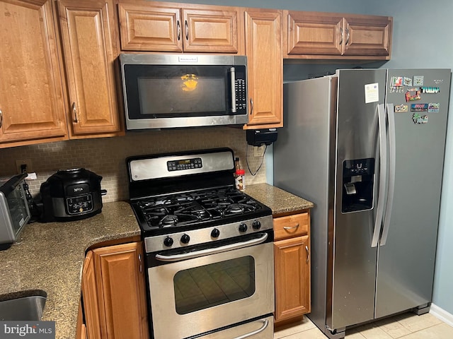 kitchen with stainless steel appliances, dark stone counters, and backsplash