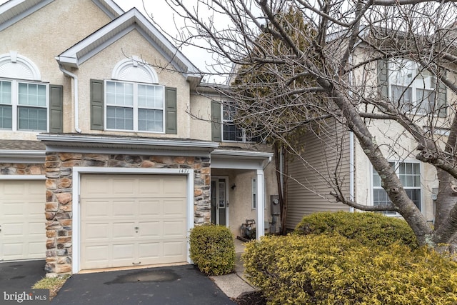 view of property with an attached garage, driveway, stone siding, and stucco siding