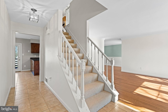 stairs featuring tile patterned flooring, an inviting chandelier, visible vents, and baseboards