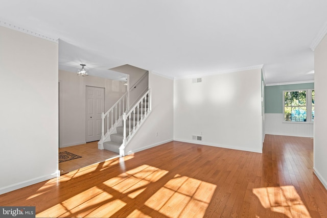 spare room featuring a wainscoted wall, visible vents, ornamental molding, hardwood / wood-style floors, and stairs