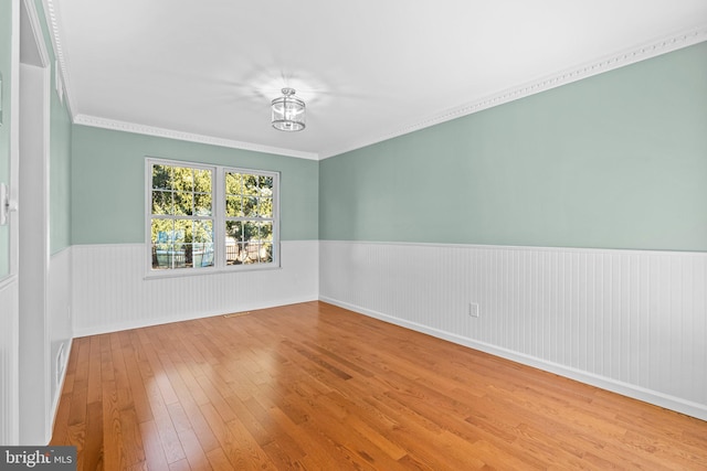 unfurnished room featuring a wainscoted wall, hardwood / wood-style floors, and crown molding