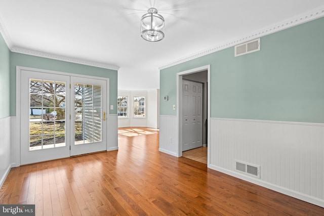 unfurnished dining area with a wainscoted wall, wood-type flooring, and visible vents