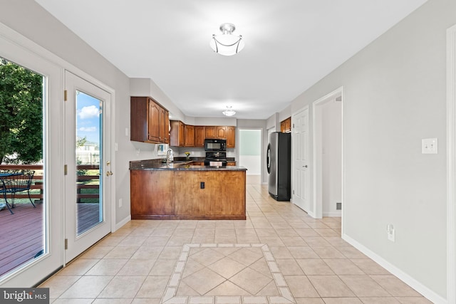 kitchen with a peninsula, light tile patterned flooring, freestanding refrigerator, a sink, and black microwave