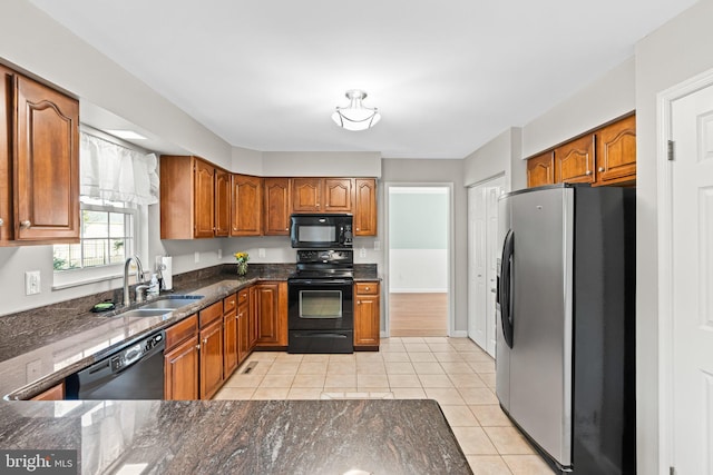 kitchen featuring brown cabinetry, dark stone countertops, black appliances, and a sink