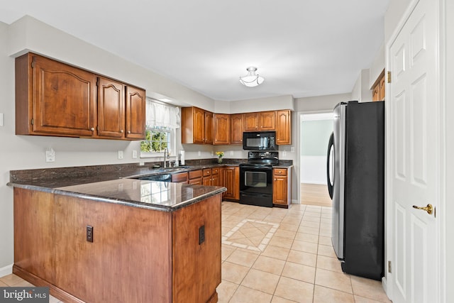 kitchen with light tile patterned floors, brown cabinetry, a peninsula, a sink, and black appliances