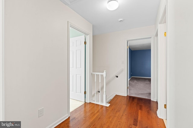 corridor with an upstairs landing, baseboards, and wood finished floors