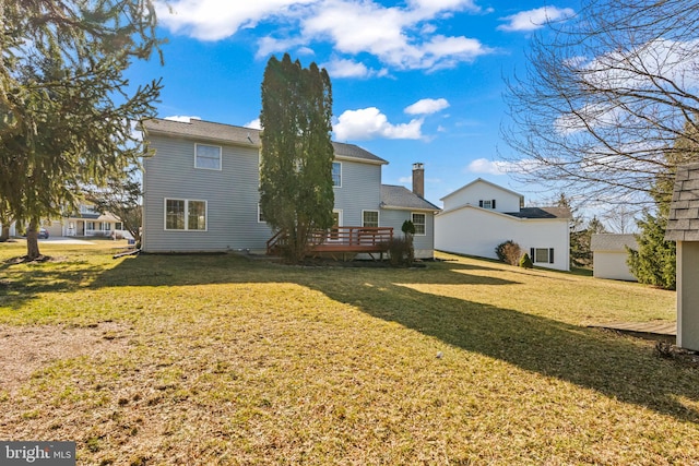 back of property with a deck, a lawn, and a chimney