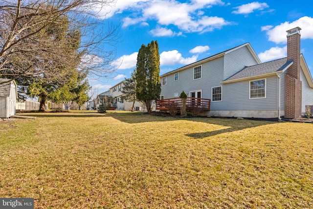 back of property featuring a wooden deck, a chimney, and a yard