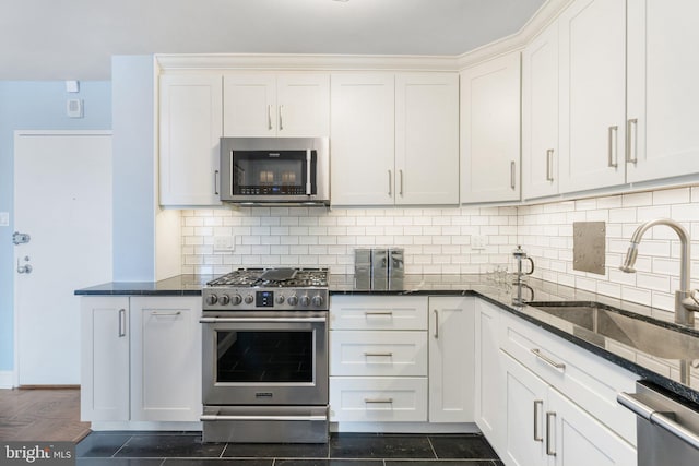 kitchen featuring white cabinetry, dark stone counters, stainless steel appliances, and a sink