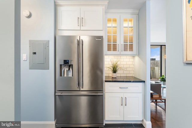 kitchen featuring high end refrigerator, electric panel, decorative backsplash, dark countertops, and glass insert cabinets