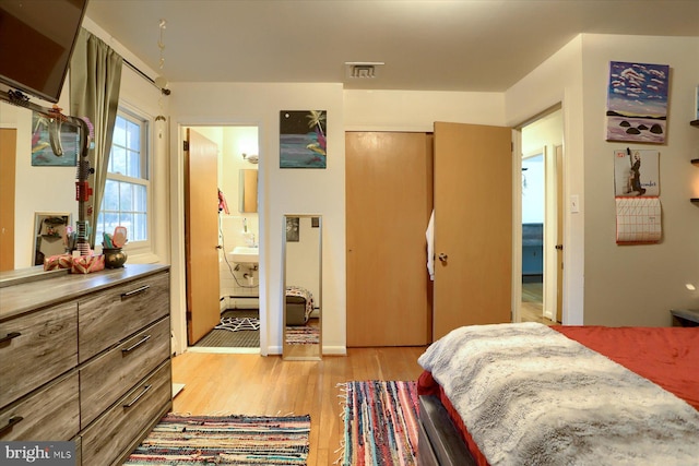 bedroom with a baseboard radiator, visible vents, a sink, and light wood finished floors