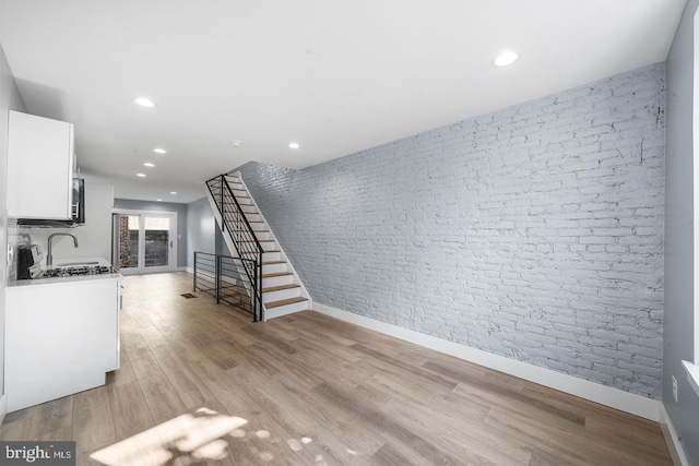 unfurnished living room with recessed lighting, light wood-style flooring, brick wall, and stairs