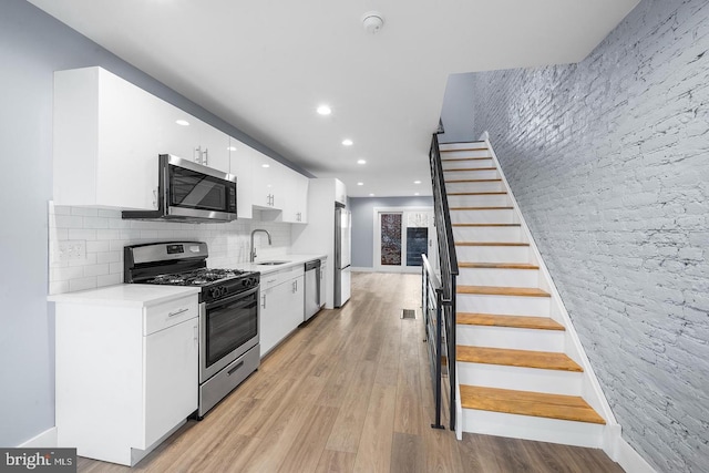 kitchen with light wood-style flooring, a sink, white cabinetry, light countertops, and appliances with stainless steel finishes