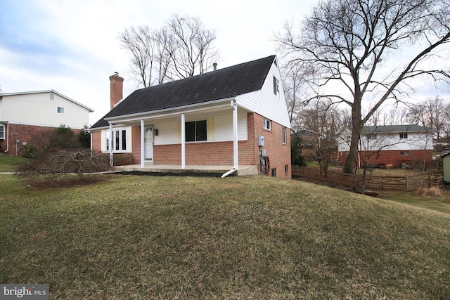 view of front of home with brick siding, a chimney, fence, a porch, and a front yard