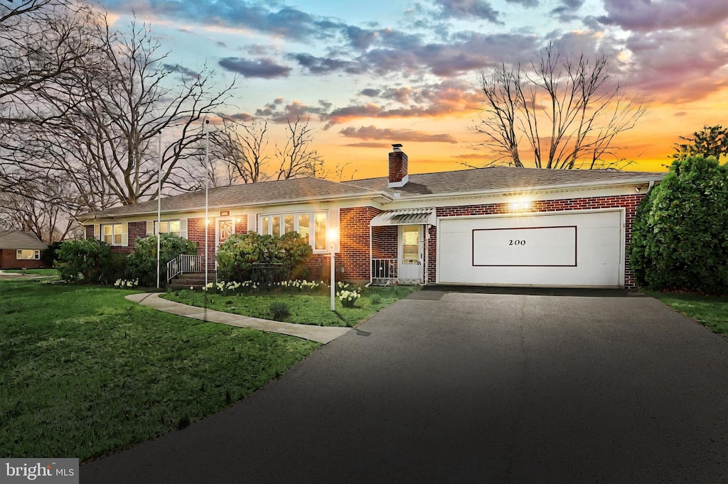 ranch-style house with a chimney, driveway, a front yard, brick siding, and a garage