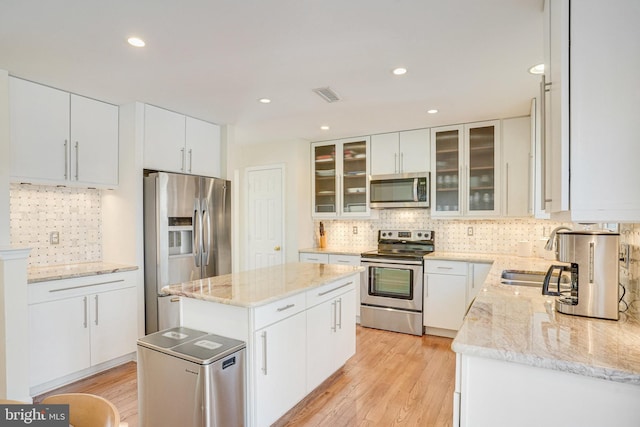 kitchen featuring stainless steel appliances, visible vents, a sink, a kitchen island, and light wood-type flooring