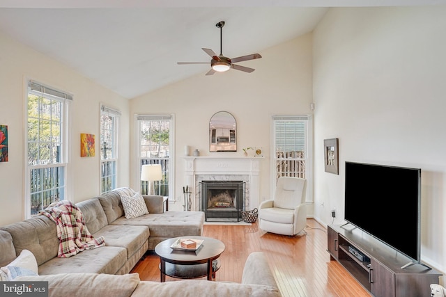 living room with high vaulted ceiling, a premium fireplace, a ceiling fan, and light wood-style floors