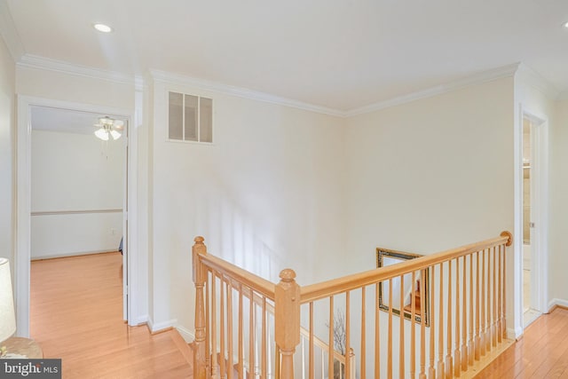 hall with wood finished floors, an upstairs landing, baseboards, visible vents, and crown molding