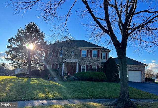 view of front facade featuring a front yard, driveway, a chimney, a garage, and brick siding