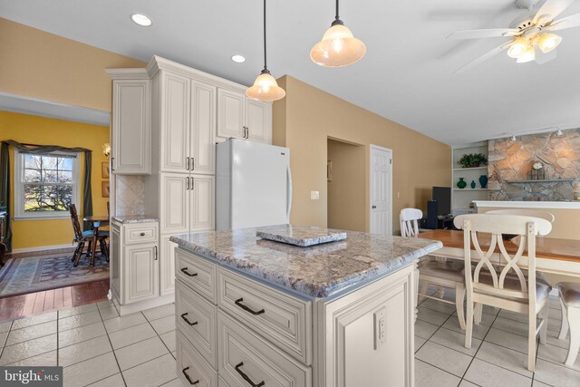 kitchen with decorative light fixtures, light stone counters, a center island, freestanding refrigerator, and decorative backsplash