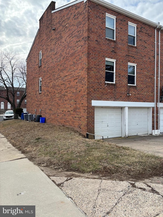 view of side of property featuring an attached garage, central air condition unit, and brick siding