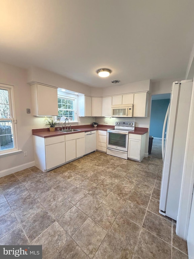 kitchen featuring dark countertops, white appliances, a sink, and baseboards