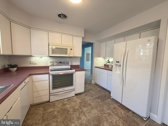 kitchen with dark countertops, white appliances, visible vents, and white cabinets