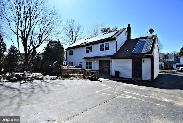 view of front of property featuring a chimney, roof mounted solar panels, and a deck