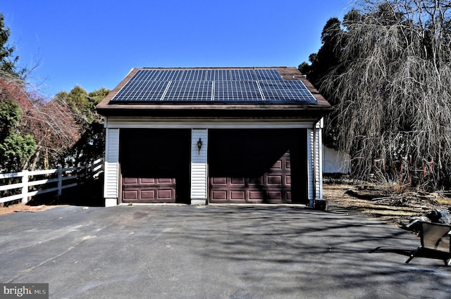 detached garage featuring roof mounted solar panels and fence