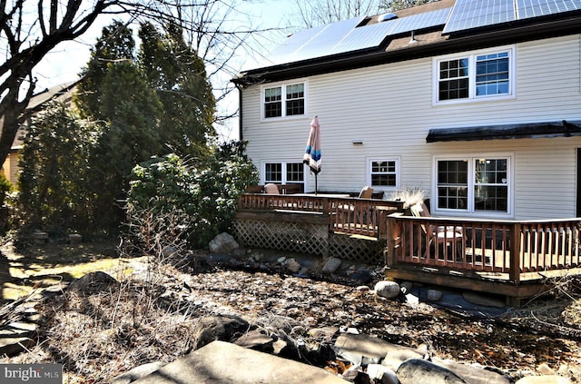 back of property with a wooden deck and solar panels