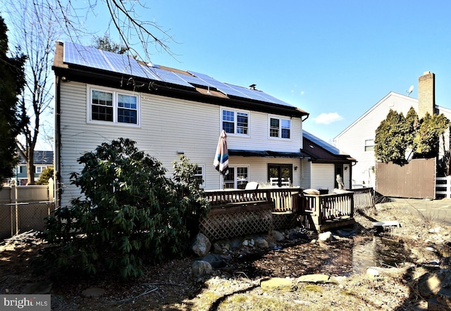 rear view of property featuring a deck, fence, and roof mounted solar panels