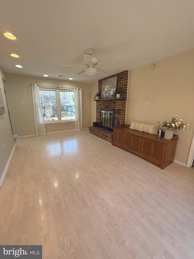 unfurnished living room with ceiling fan, a brick fireplace, wood finished floors, and baseboards