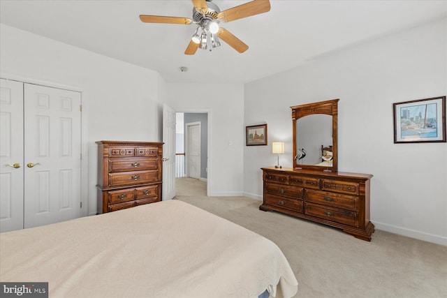 bedroom with a closet, light colored carpet, baseboards, and ceiling fan