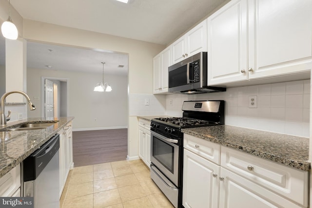 kitchen featuring stainless steel appliances, backsplash, white cabinets, a sink, and dark stone countertops