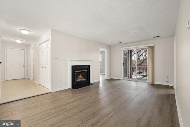 unfurnished living room featuring a fireplace with flush hearth, a textured ceiling, baseboards, and wood finished floors